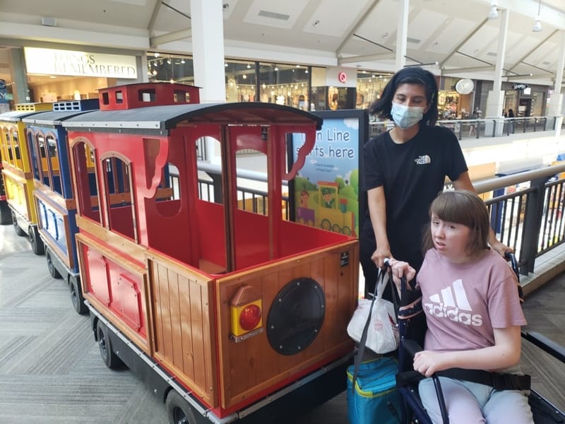 A colorful miniature train in a shopping mall with people nearby.