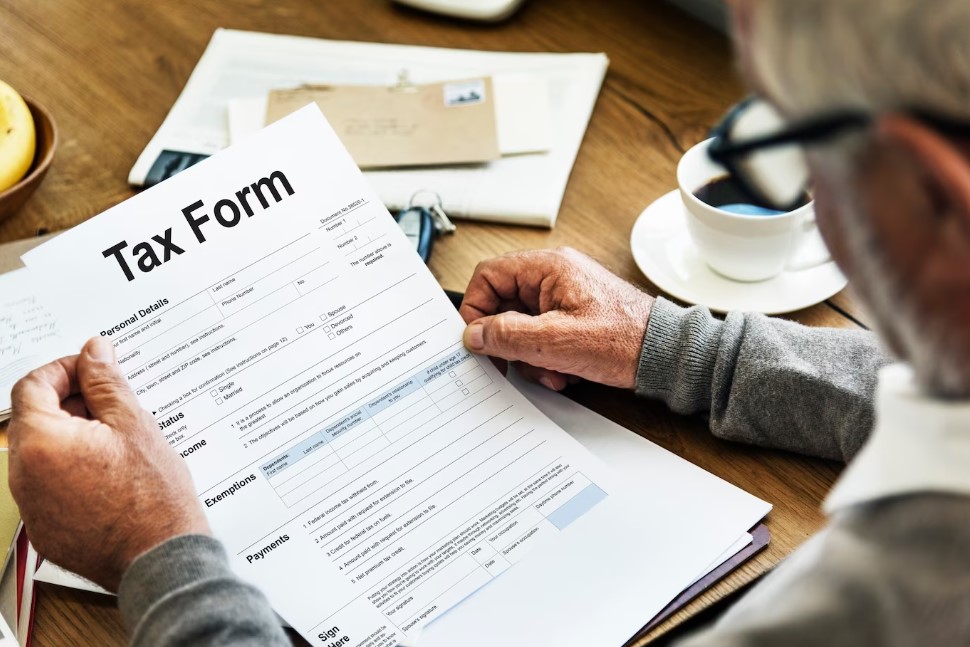 Person holding a tax form on a desk with a cup of coffee and eyeglasses nearby.