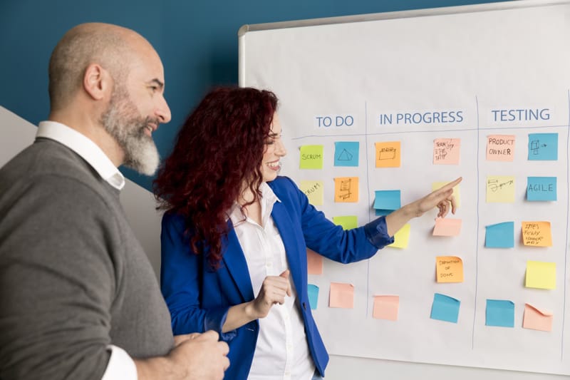 Two professionals discussing a Kanban board with sticky notes.