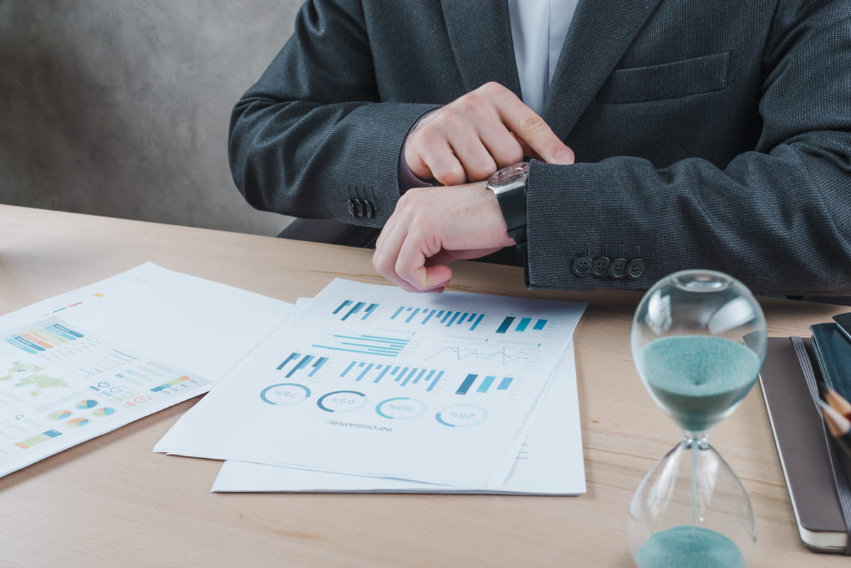 Businessperson reviewing charts and graphs with a sand timer on the table.