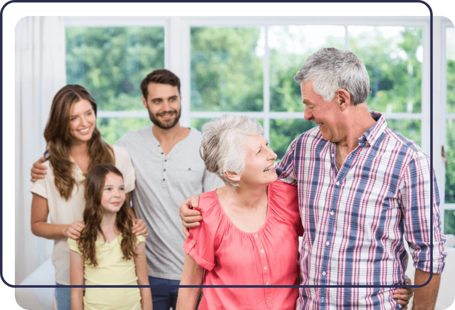 Family gathering with five members standing together indoors, smiling, with a bright window background.