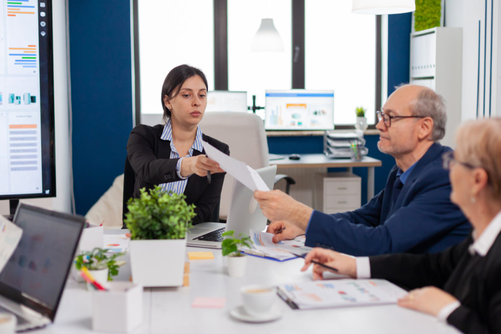 Professionals in a meeting room with documents and laptops, discussing work.