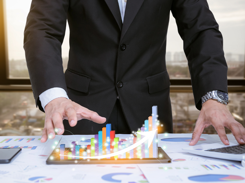 Businessman analyzing holographic financial charts on a digital tablet over paperwork.