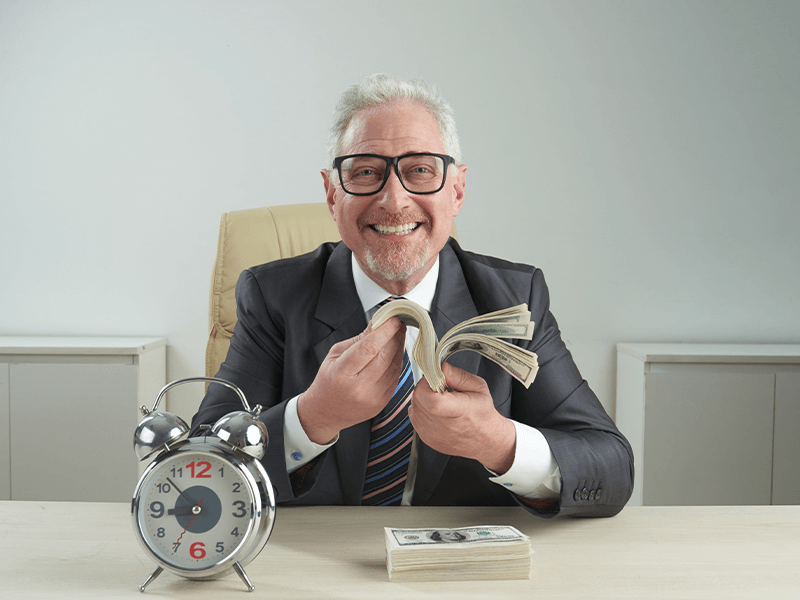 Person in a suit counting money at a desk with a clock beside them.