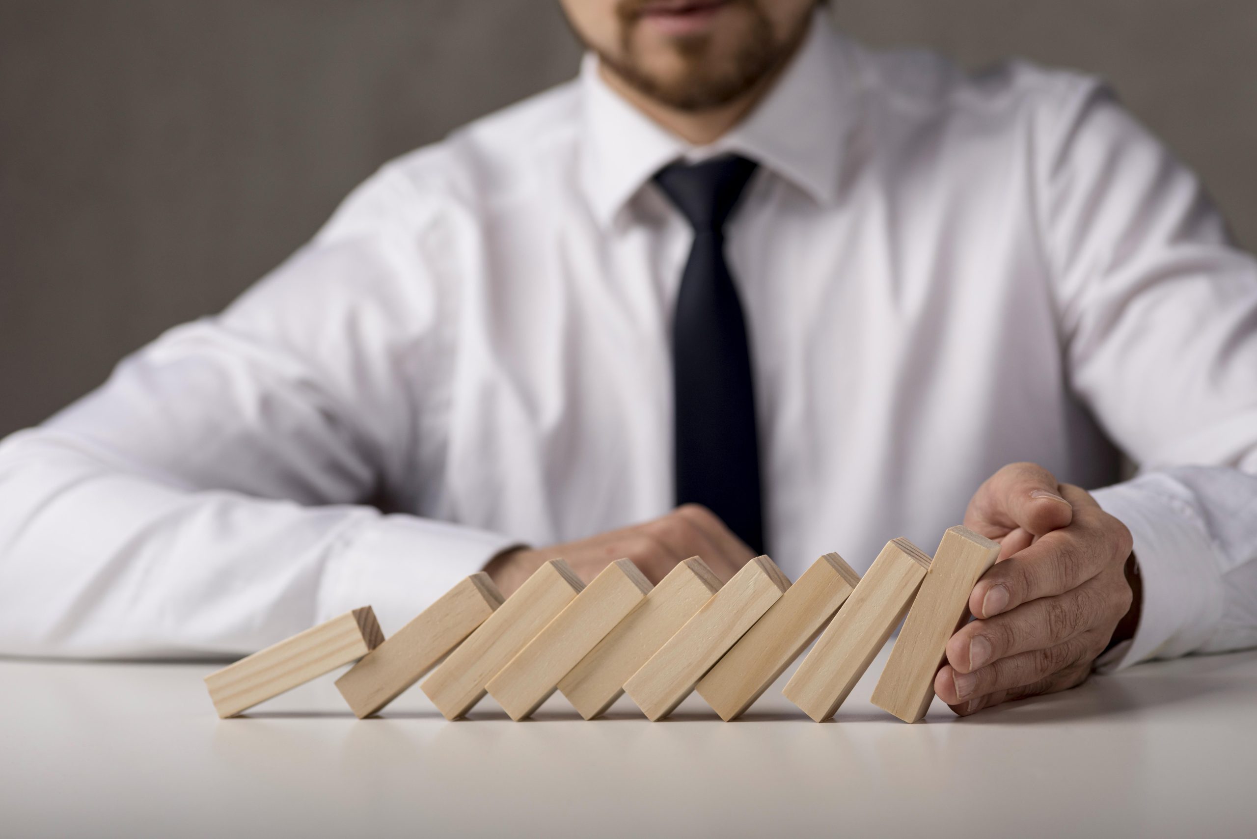 Man in a white shirt stopping a row of falling wooden blocks on a table.