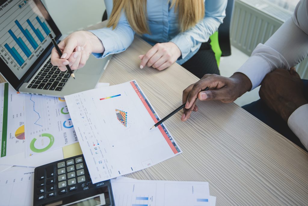 Three people analyzing data with charts and a laptop on a desk.