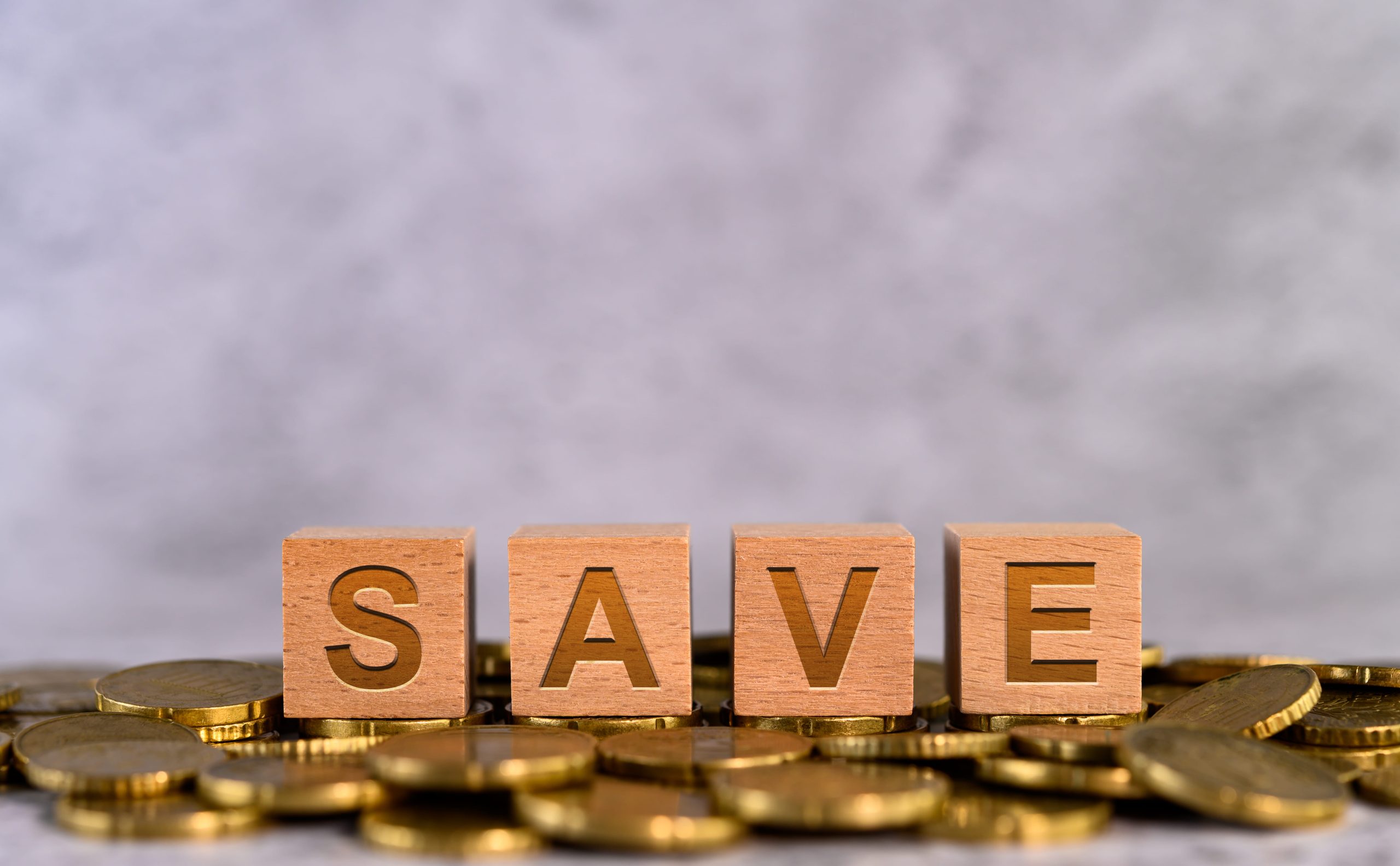 Wooden blocks spelling "SAVE" on a background of scattered coins.