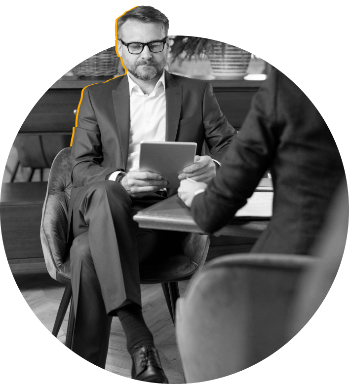 Person in suit holding a tablet with another person partially visible in foreground. Black and white image.