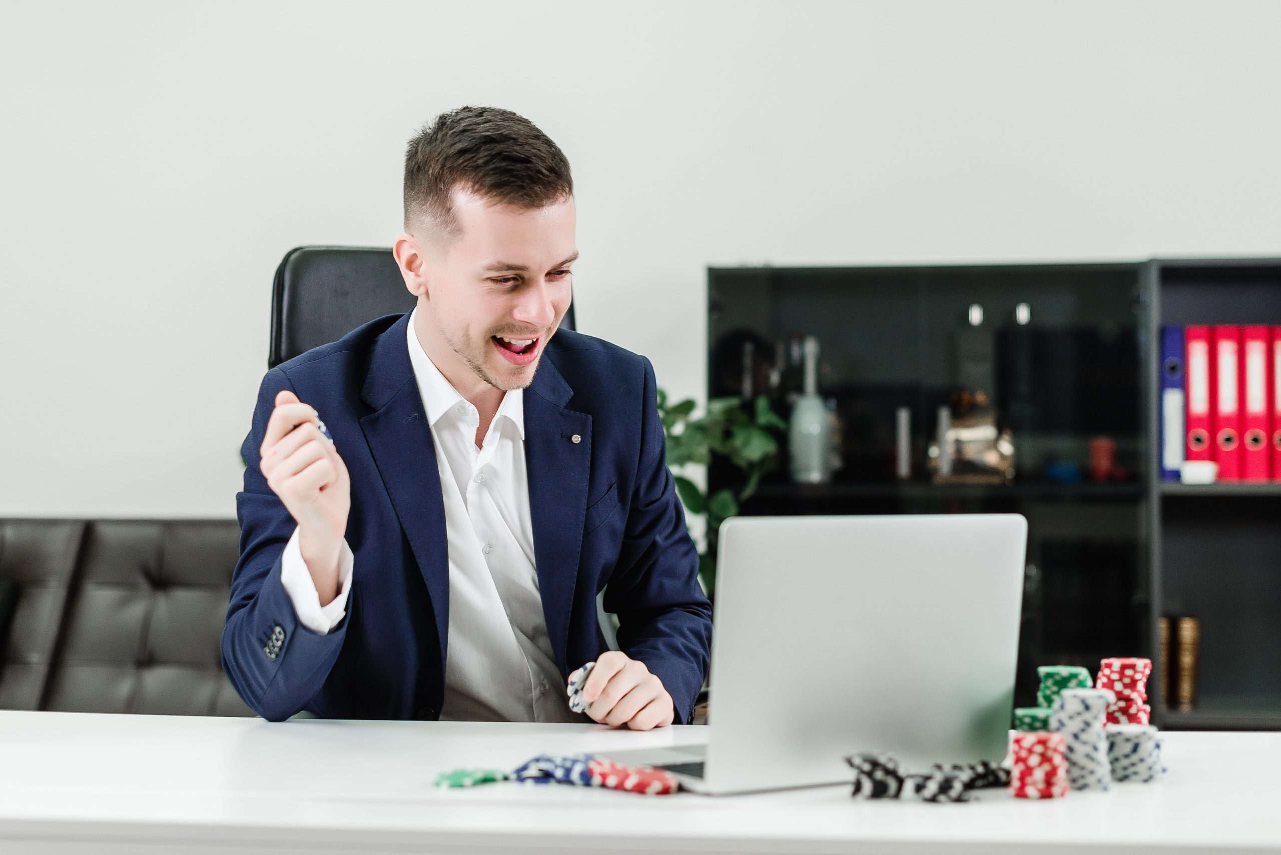 Person in a suit at a desk with a laptop and stacks of poker chips.
