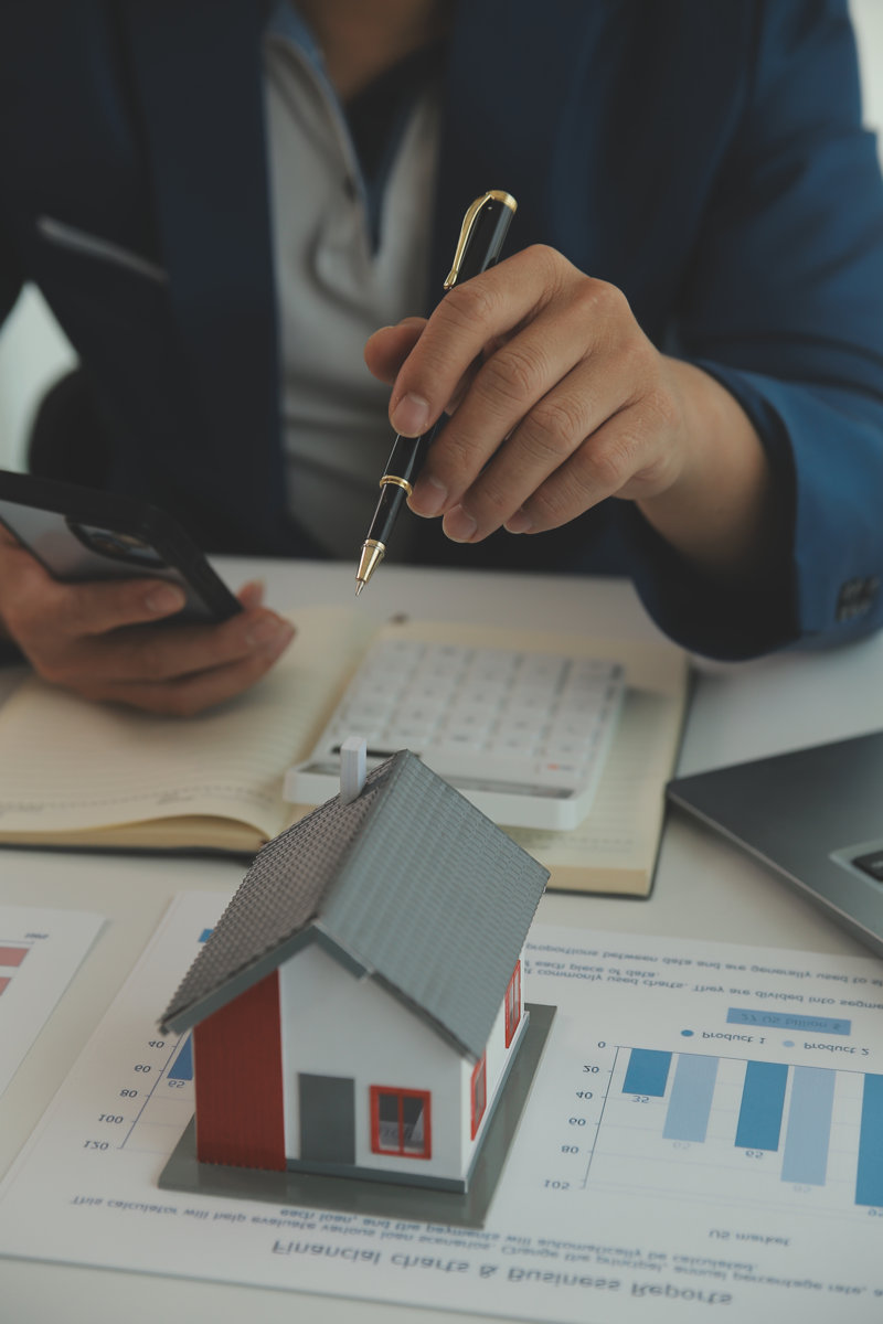 Person holding a pen over charts with a model house on the table.