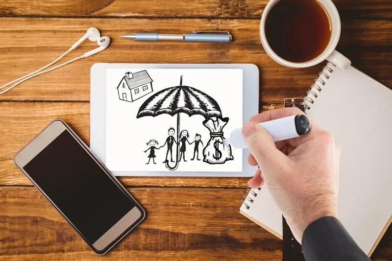 Hand drawing insurance concept with family, house, and money under umbrella on tablet, wooden desk.
