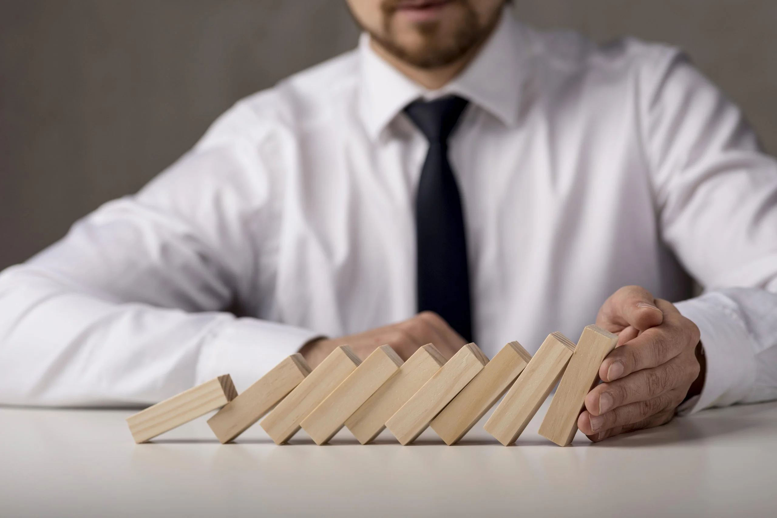 Man in a white shirt stopping a row of falling wooden blocks on a table.