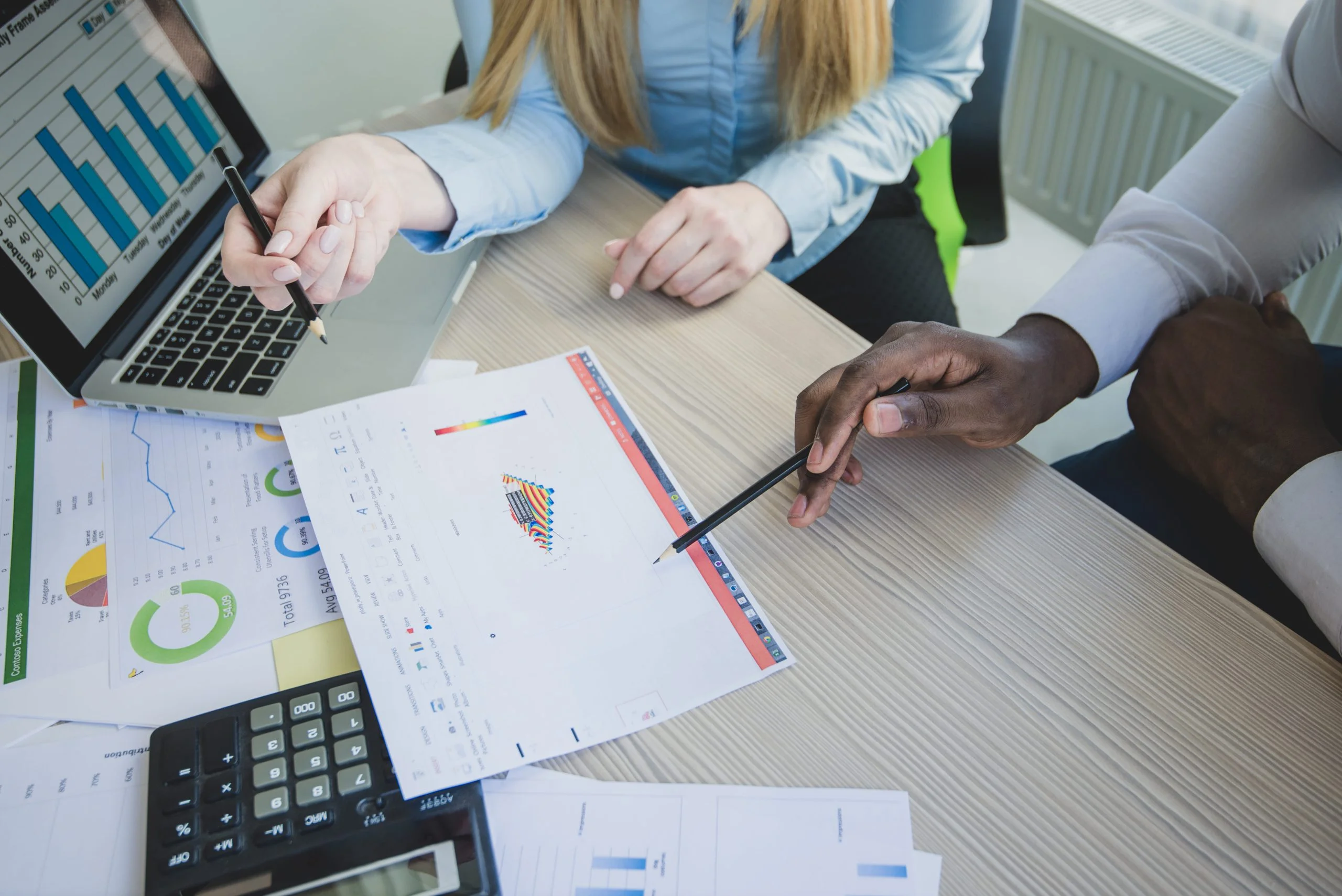 Three people analyzing data with charts and a laptop on a desk.