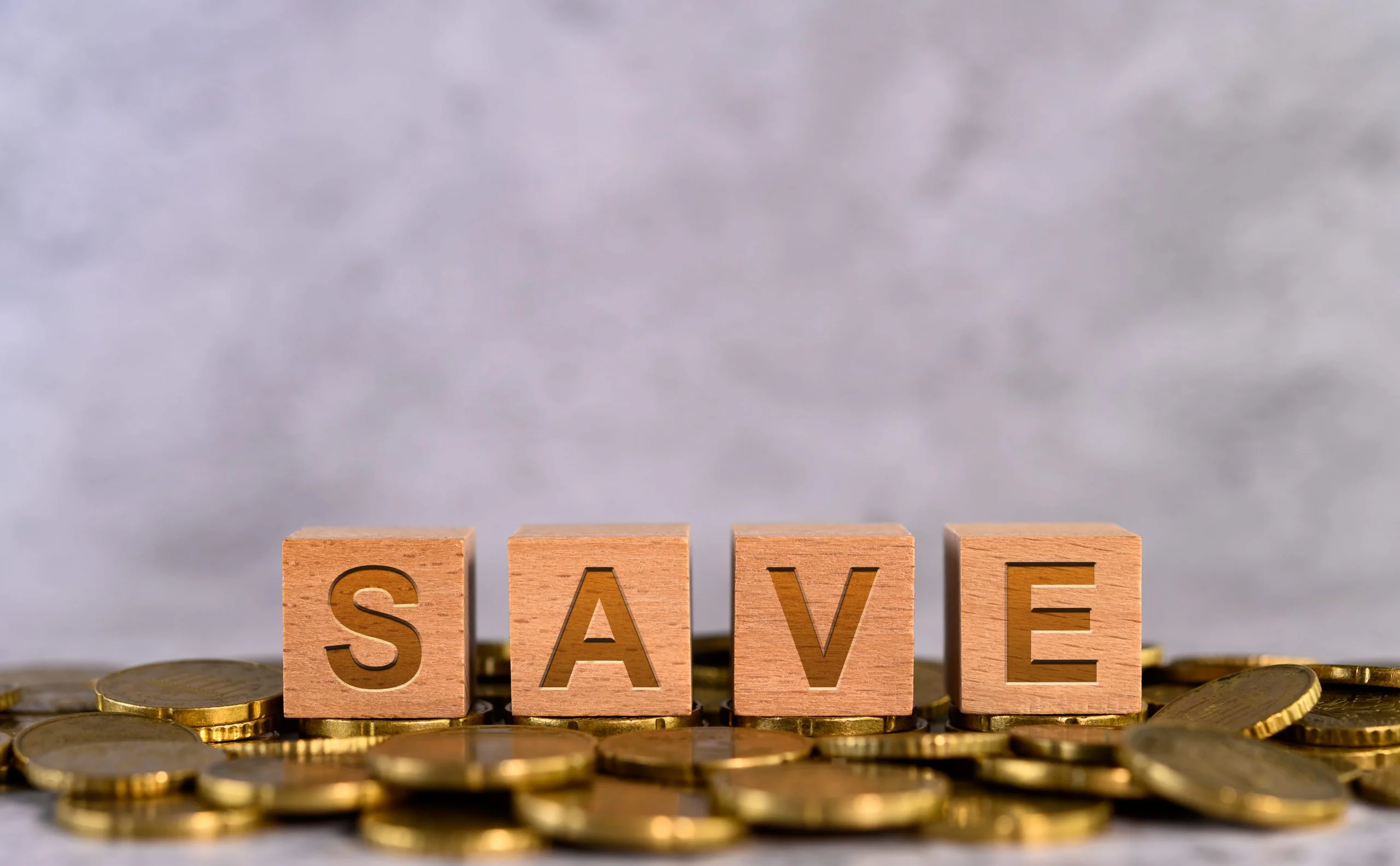 Wooden blocks spelling "SAVE" on a background of scattered coins.